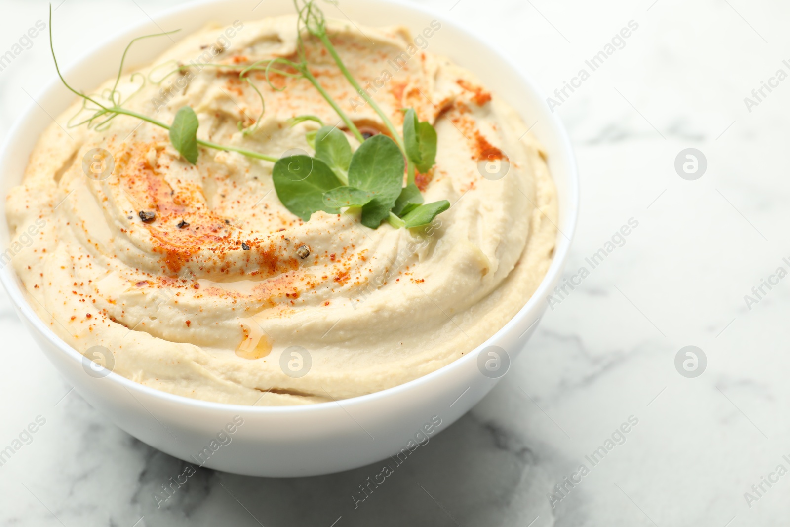 Photo of Delicious hummus with paprika in bowl on white marble table, closeup