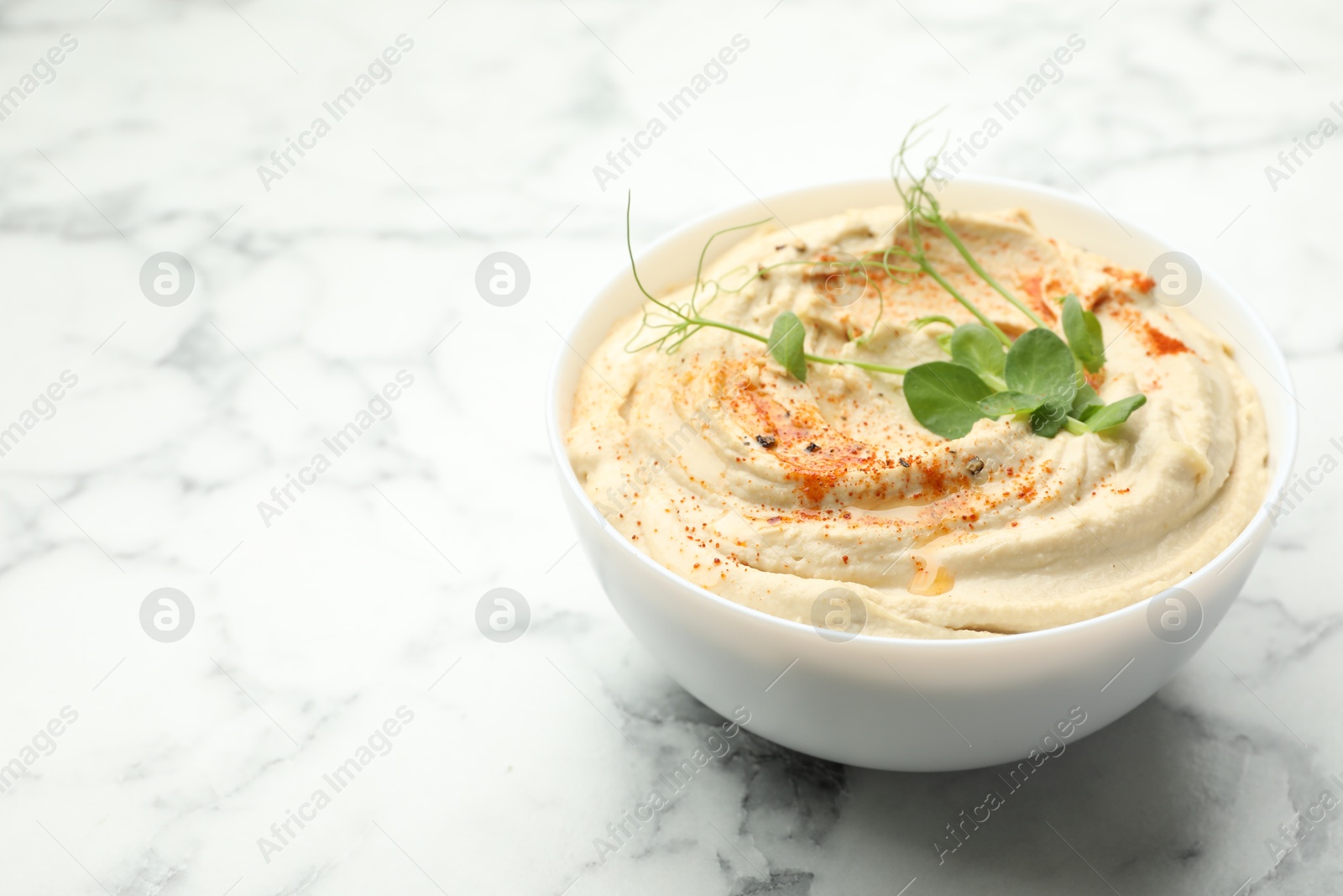 Photo of Delicious hummus with paprika in bowl on white marble table, closeup. Space for text