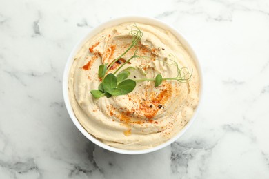 Photo of Delicious hummus with paprika in bowl on white marble table, top view