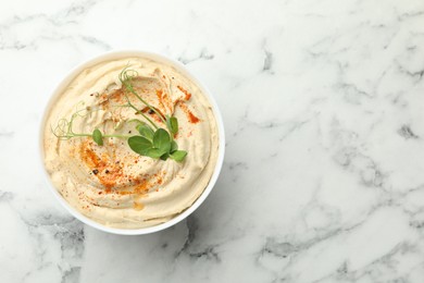 Photo of Delicious hummus with paprika in bowl on white marble table, top view. Space for text