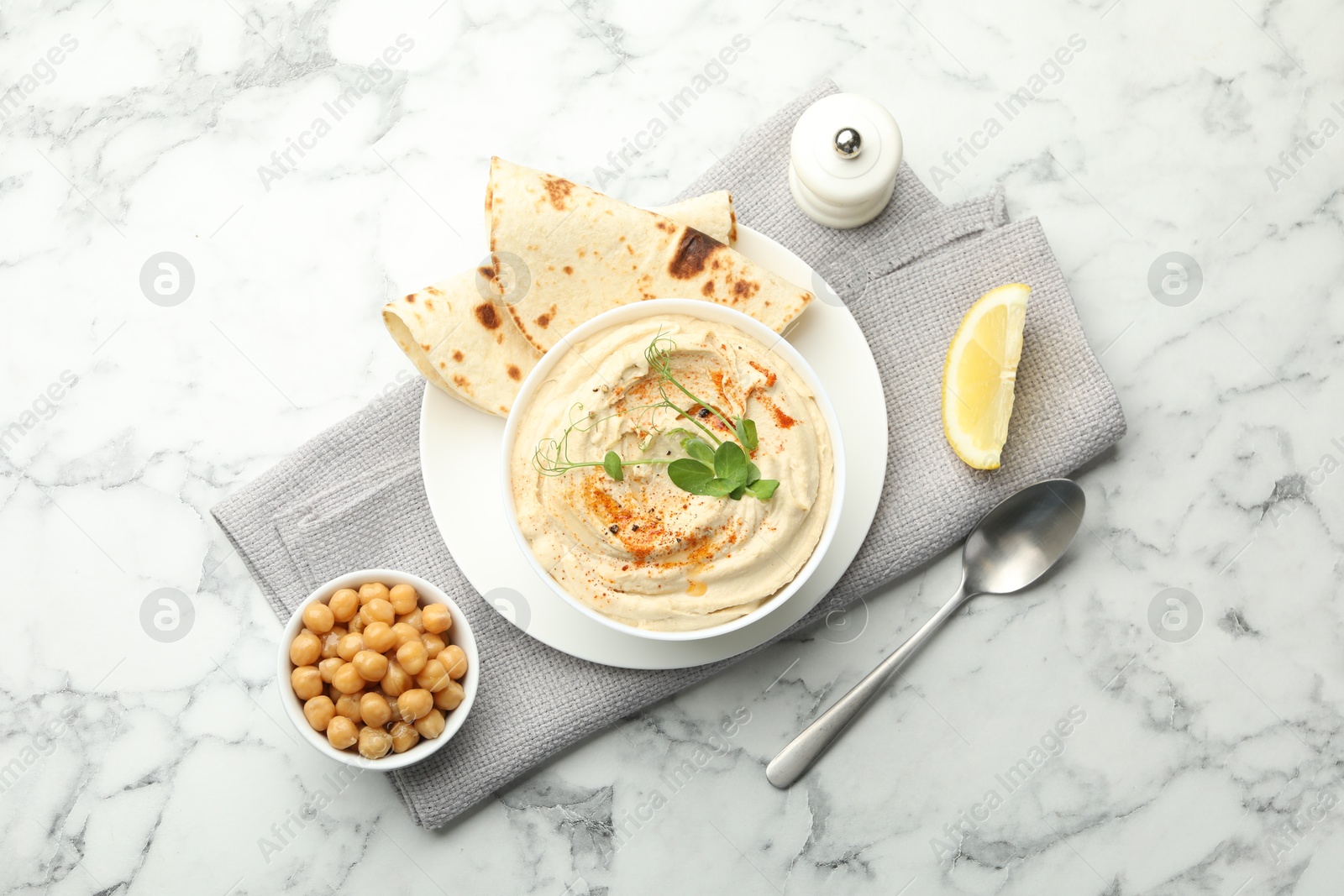 Photo of Delicious hummus with paprika, pita and chickpeas on white marble table, top view