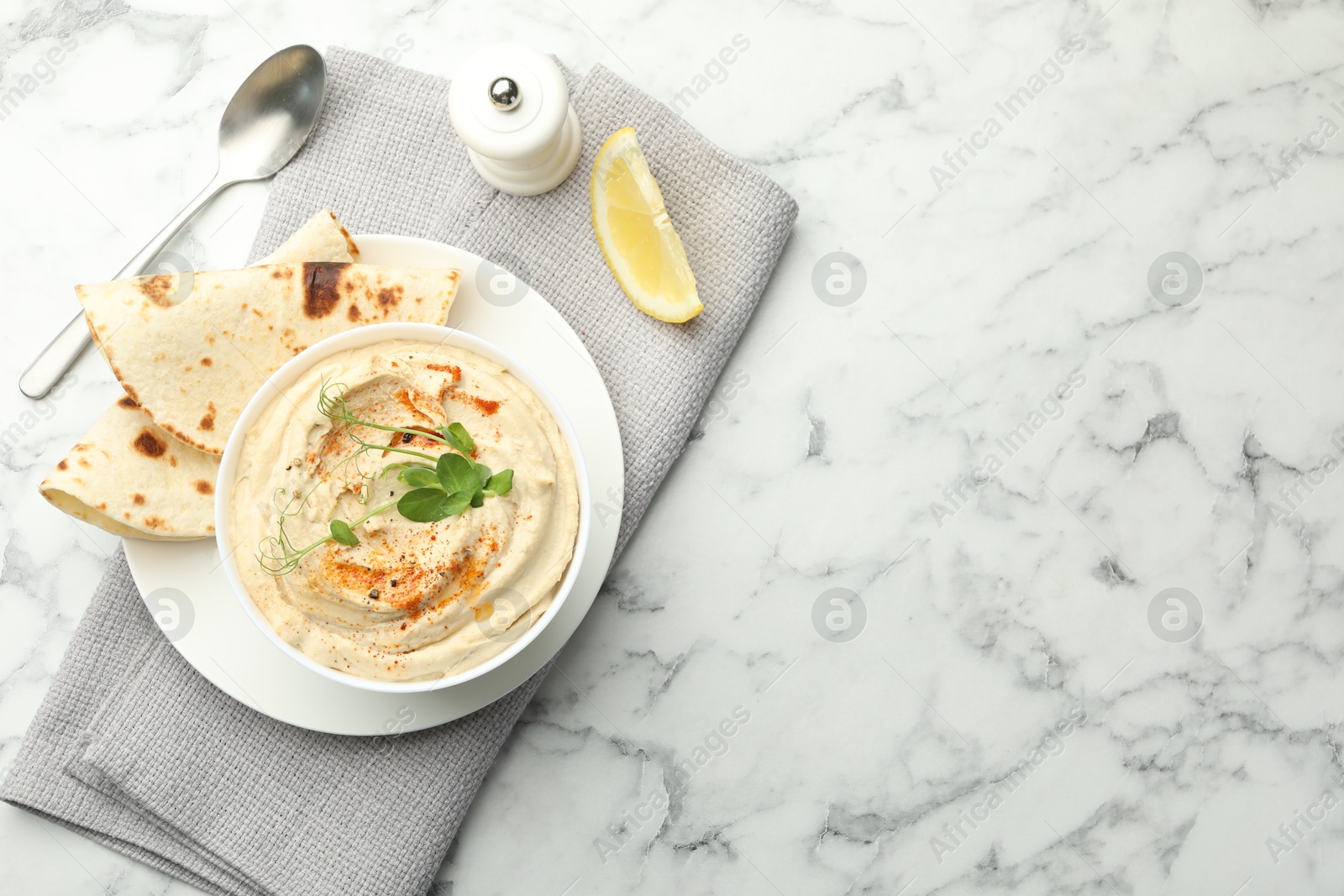 Photo of Delicious hummus with paprika, pita and lemon on white marble table, top view. Space for text