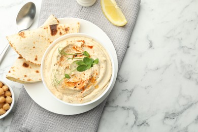 Photo of Delicious hummus with paprika, pita and chickpeas on white marble table, top view. Space for text