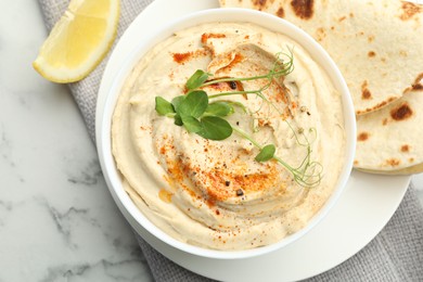 Photo of Delicious hummus with paprika, pita and lemon on white marble table, top view