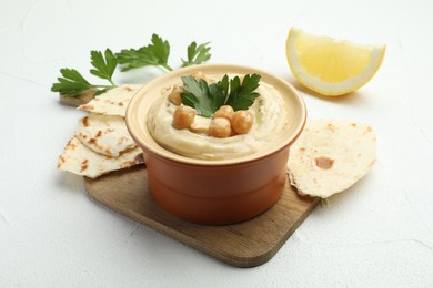 Photo of Delicious hummus with parsley, chickpeas, pita and lemon on white table, closeup