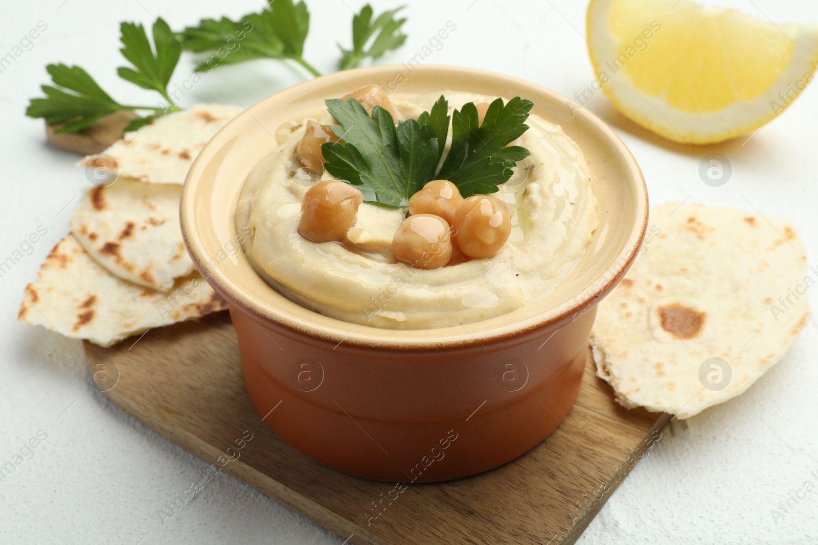 Photo of Delicious hummus with parsley, chickpeas, pita and lemon on white table, closeup