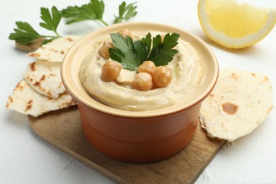 Photo of Delicious hummus with parsley, chickpeas, pita and lemon on white table, closeup