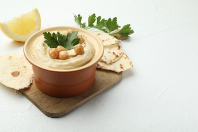 Photo of Delicious hummus with parsley, chickpeas, pita and lemon on white table, closeup. Space for text