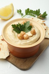 Photo of Delicious hummus with parsley, chickpeas, pita and lemon on white table, closeup