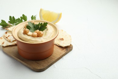 Photo of Delicious hummus with parsley, chickpeas, pita and lemon on white table, closeup. Space for text