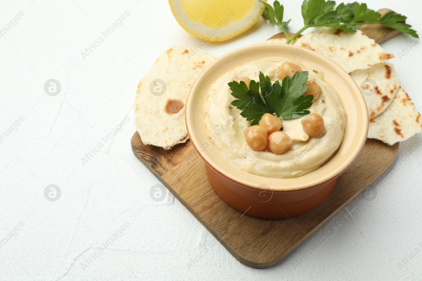 Photo of Delicious hummus with parsley, chickpeas, pita and lemon on white table, closeup