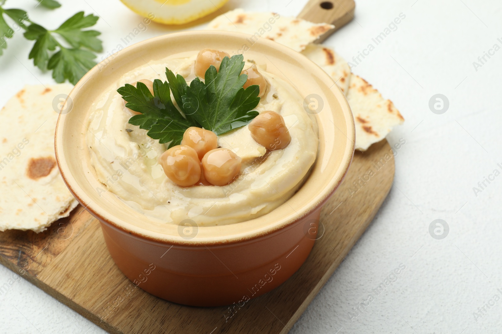 Photo of Delicious hummus with parsley, chickpeas and pita on white table, closeup