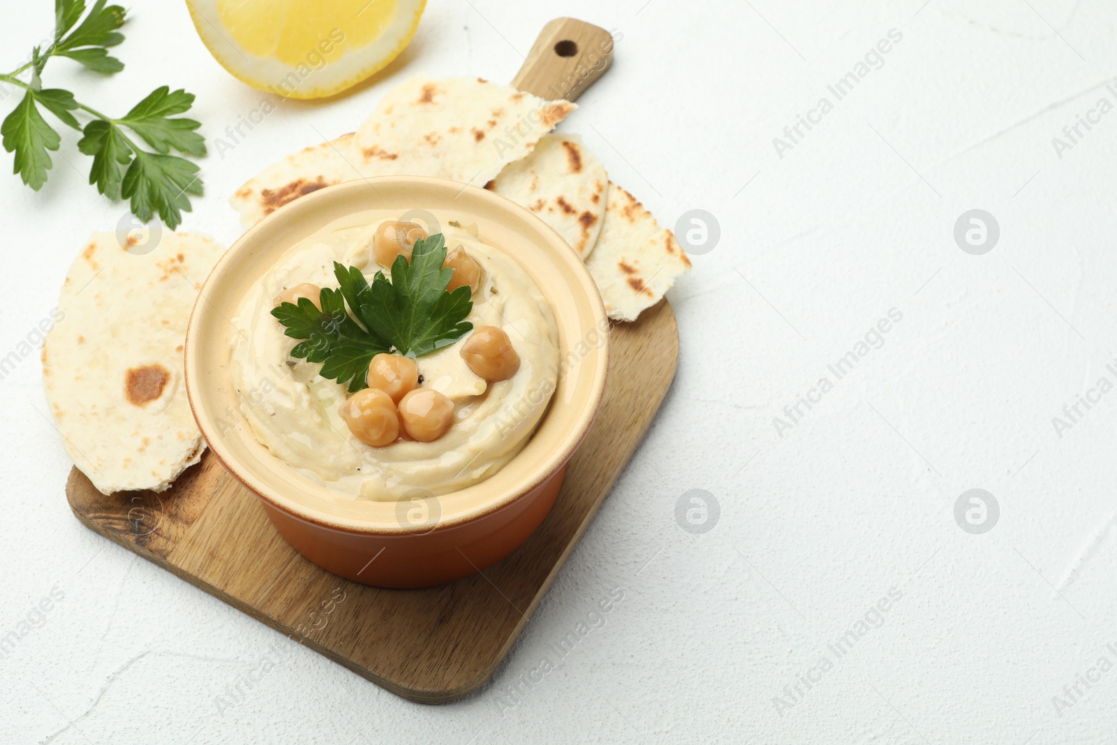 Photo of Delicious hummus with parsley, chickpeas and pita on white table, closeup. Space for text