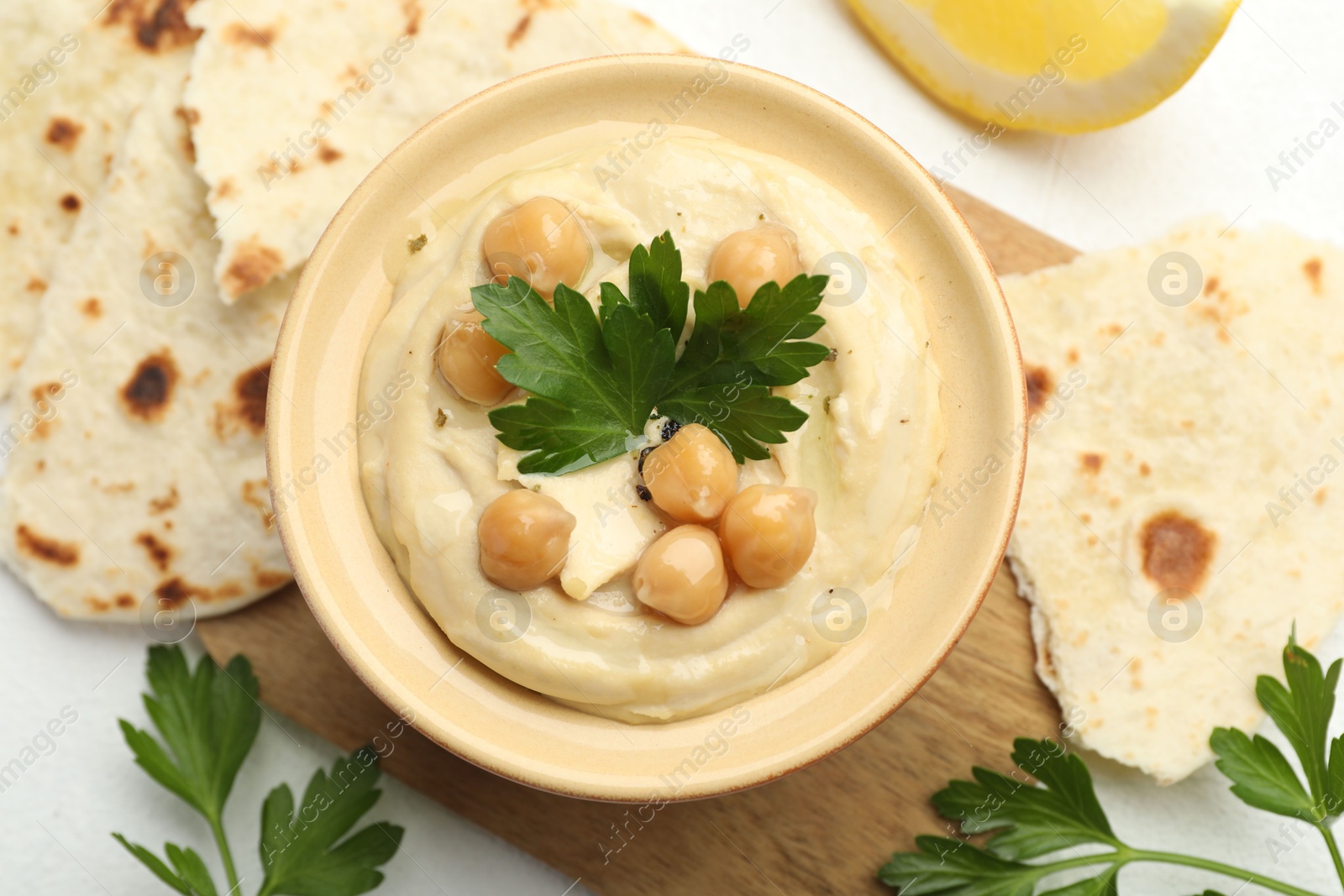 Photo of Delicious hummus with parsley, chickpeas and pita on white table, top view