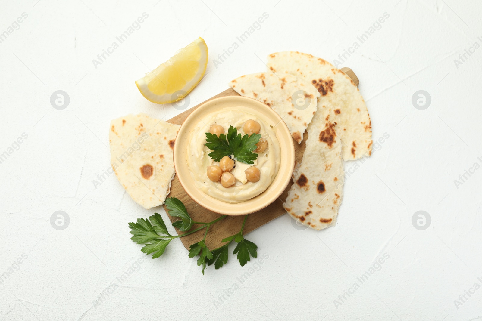 Photo of Delicious hummus with parsley, chickpeas, lemon and pita on white table, top view