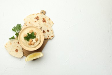 Photo of Delicious hummus with parsley, chickpeas, lemon and pita on white table, top view. Space for text