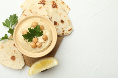 Photo of Delicious hummus with parsley, chickpeas, lemon and pita on white table, top view. Space for text