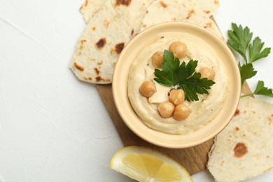 Photo of Delicious hummus with parsley, chickpeas, lemon and pita on white table, top view. Space for text