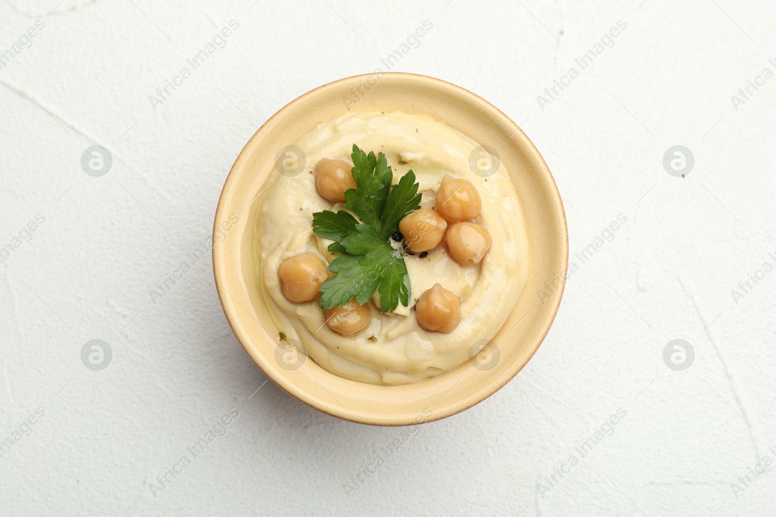 Photo of Delicious hummus with parsley and chickpeas in bowl on white table, top view