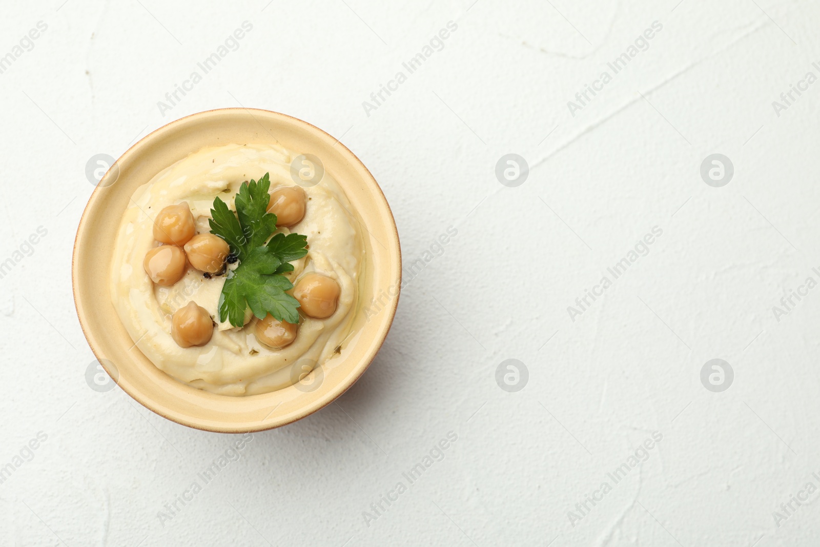 Photo of Delicious hummus with parsley and chickpeas in bowl on white table, top view. Space for text