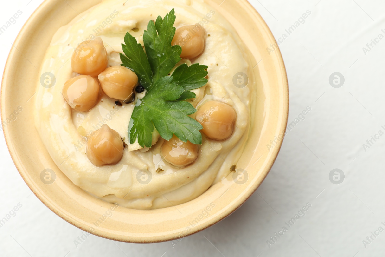 Photo of Delicious hummus with parsley and chickpeas in bowl on white table, top view