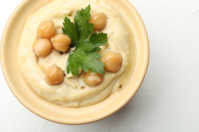 Photo of Delicious hummus with parsley and chickpeas in bowl on white table, top view