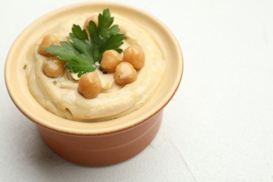 Photo of Delicious hummus with parsley and chickpeas in bowl on white table, closeup