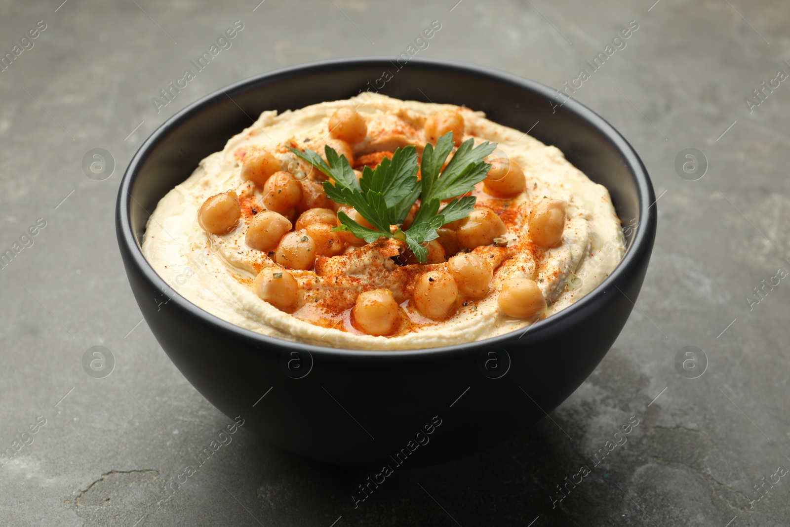 Photo of Delicious hummus with parsley, paprika and chickpeas in bowl on grey table, closeup