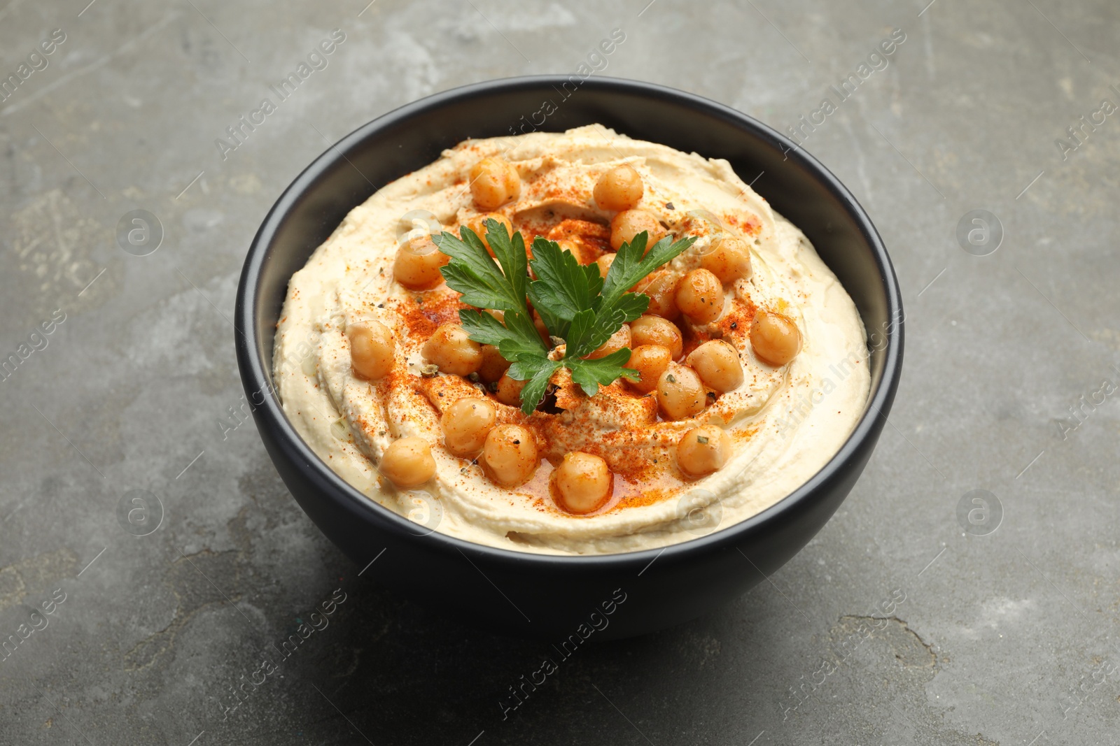 Photo of Delicious hummus with parsley, paprika and chickpeas in bowl on grey table, closeup