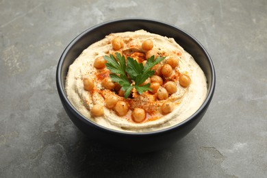 Photo of Delicious hummus with parsley, paprika and chickpeas in bowl on grey table, closeup