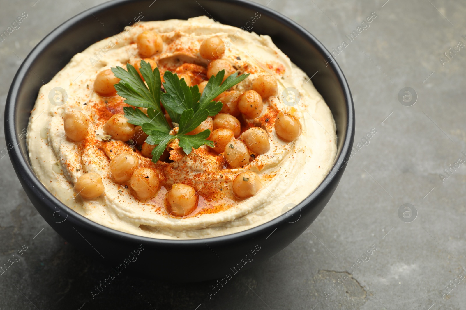 Photo of Delicious hummus with parsley, paprika and chickpeas in bowl on grey table, closeup