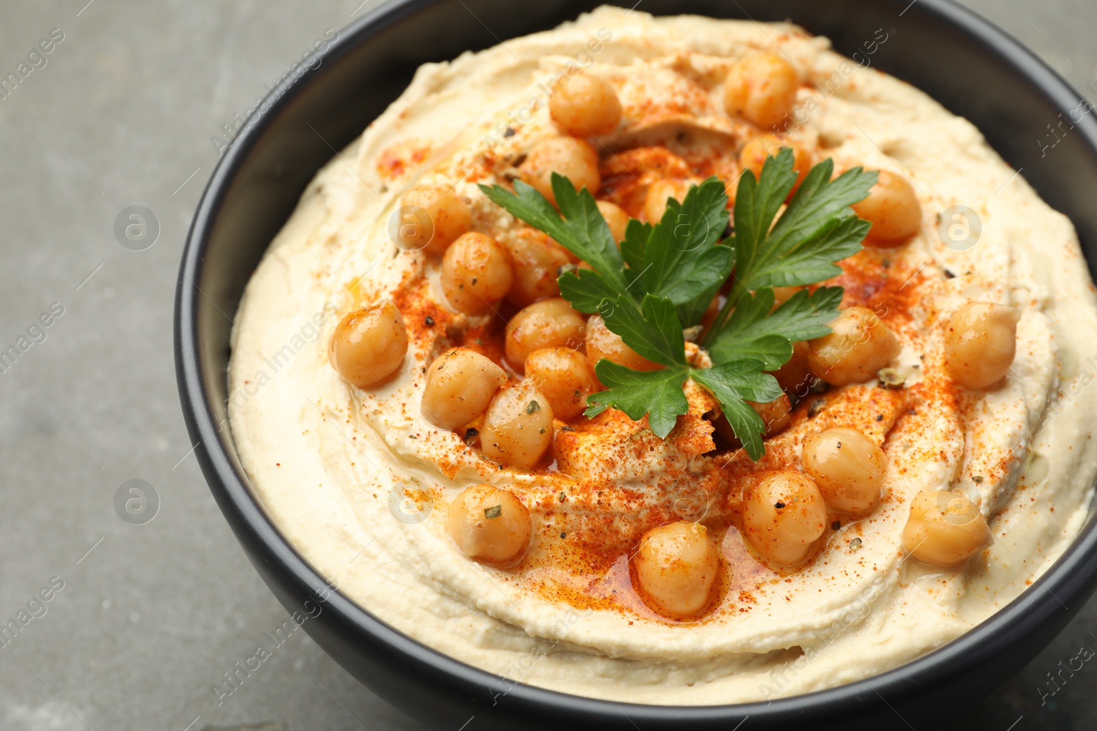 Photo of Delicious hummus with parsley, paprika and chickpeas in bowl on grey table, closeup