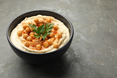 Photo of Delicious hummus with parsley, paprika and chickpeas in bowl on grey table, closeup. Space for text