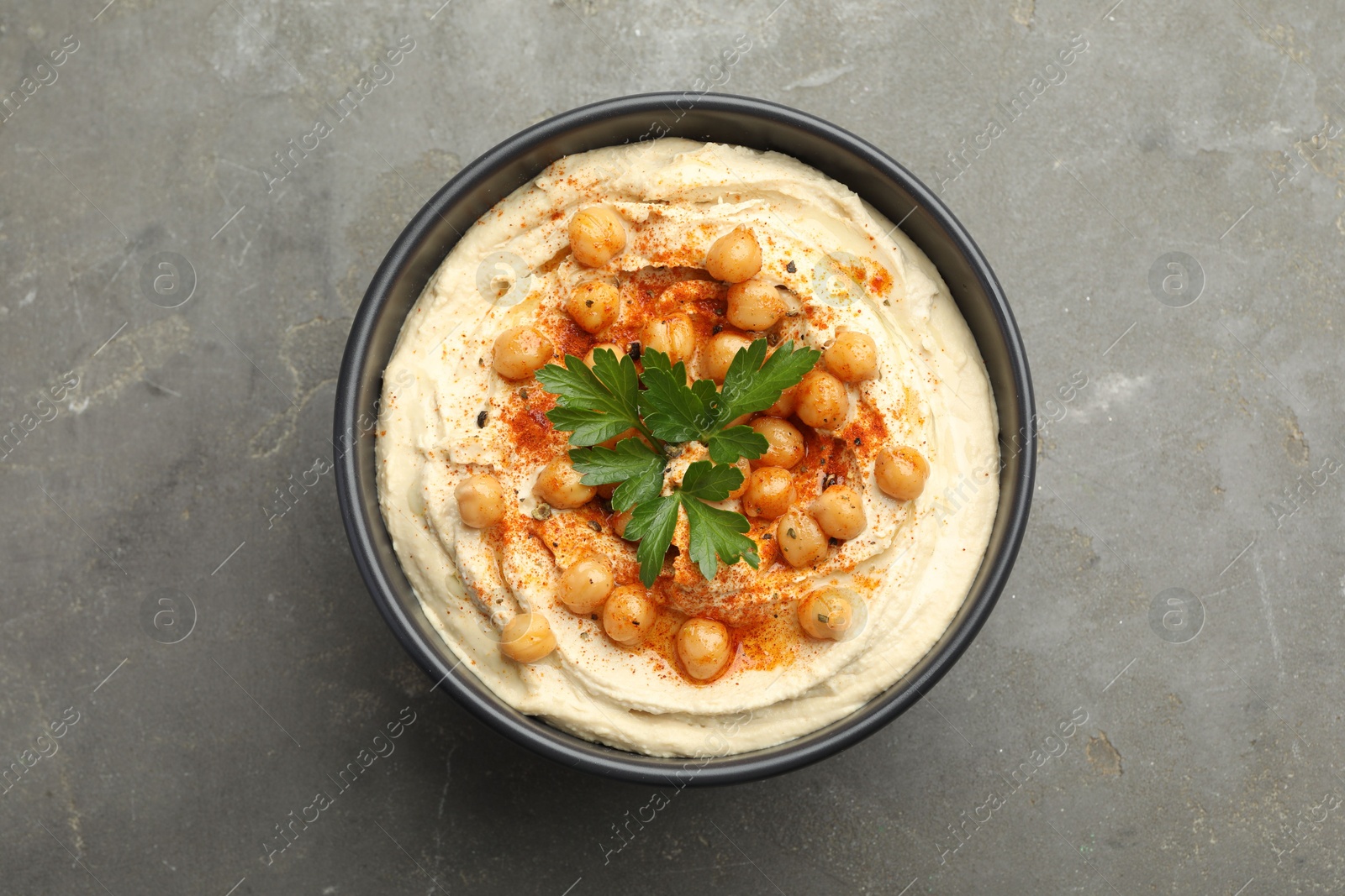 Photo of Delicious hummus with parsley, paprika and chickpeas in bowl on grey table, top view