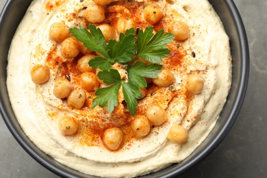 Photo of Delicious hummus with parsley, paprika and chickpeas in bowl on grey table, closeup