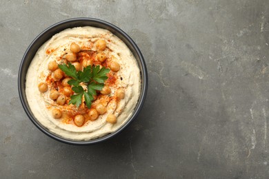 Photo of Delicious hummus with parsley, paprika and chickpeas in bowl on grey table, top view. Space for text