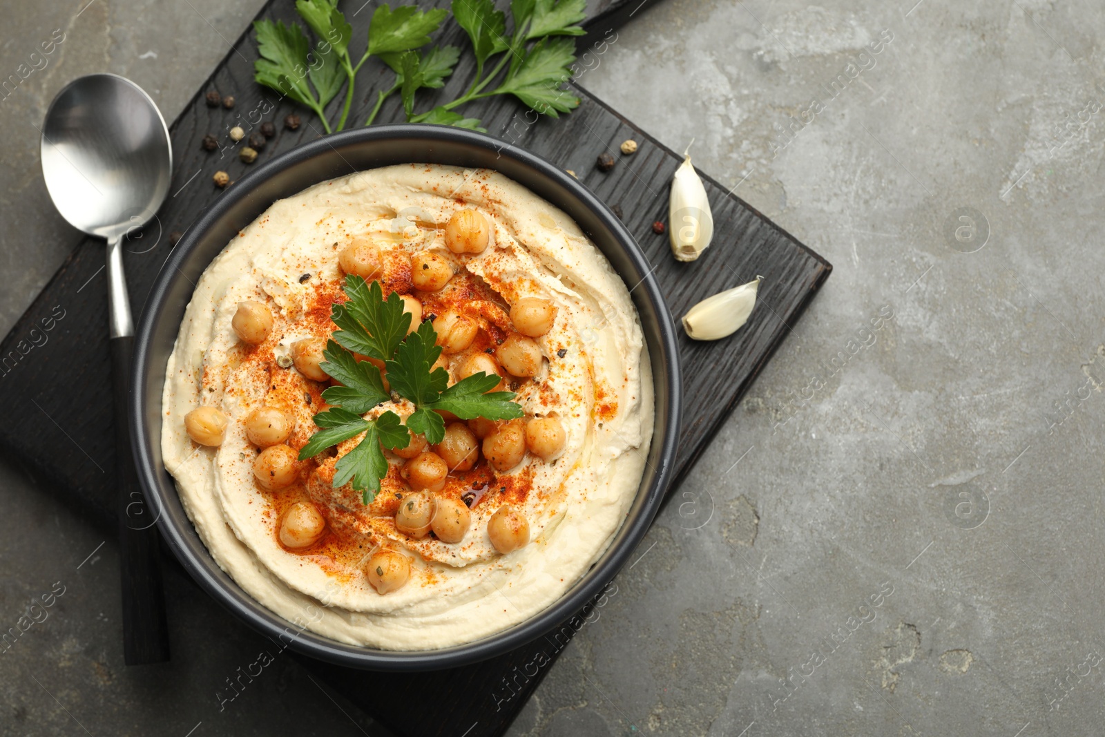 Photo of Delicious hummus with parsley, paprika and chickpeas on grey table, top view