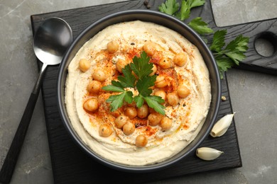 Photo of Delicious hummus with parsley, paprika and chickpeas on grey table, top view