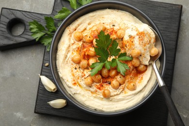 Photo of Delicious hummus with parsley, paprika and chickpeas on grey table, top view