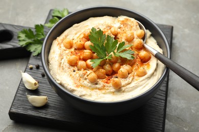 Photo of Delicious hummus with parsley, paprika and chickpeas on grey table, closeup