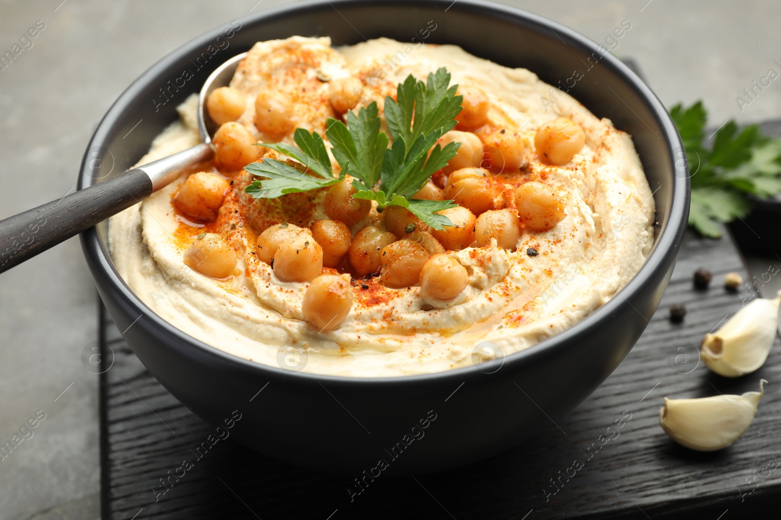 Photo of Delicious hummus with parsley, paprika and chickpeas on grey table, closeup