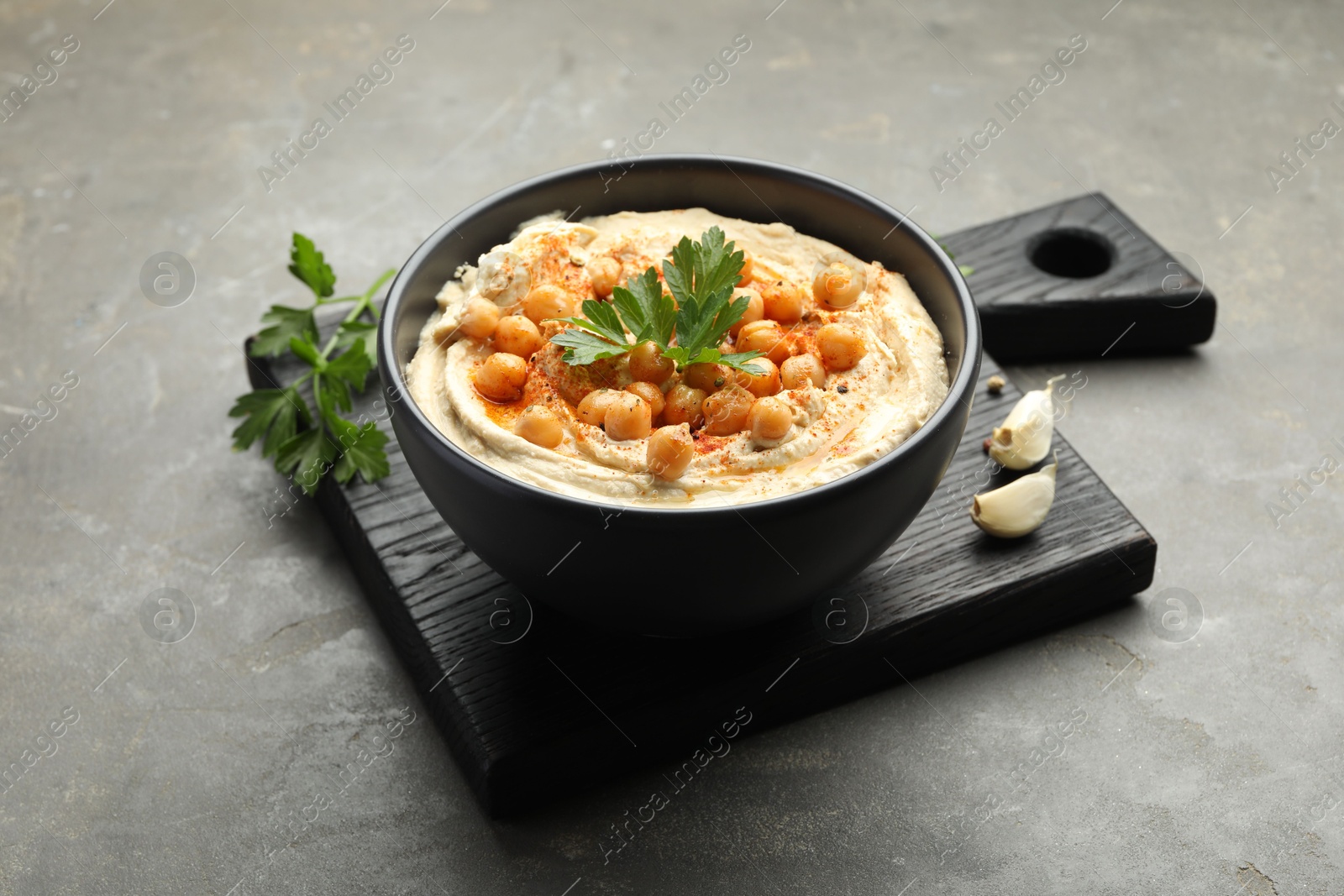 Photo of Delicious hummus with parsley, paprika and chickpeas on grey table