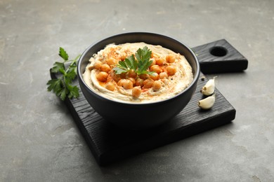 Photo of Delicious hummus with parsley, paprika and chickpeas on grey table