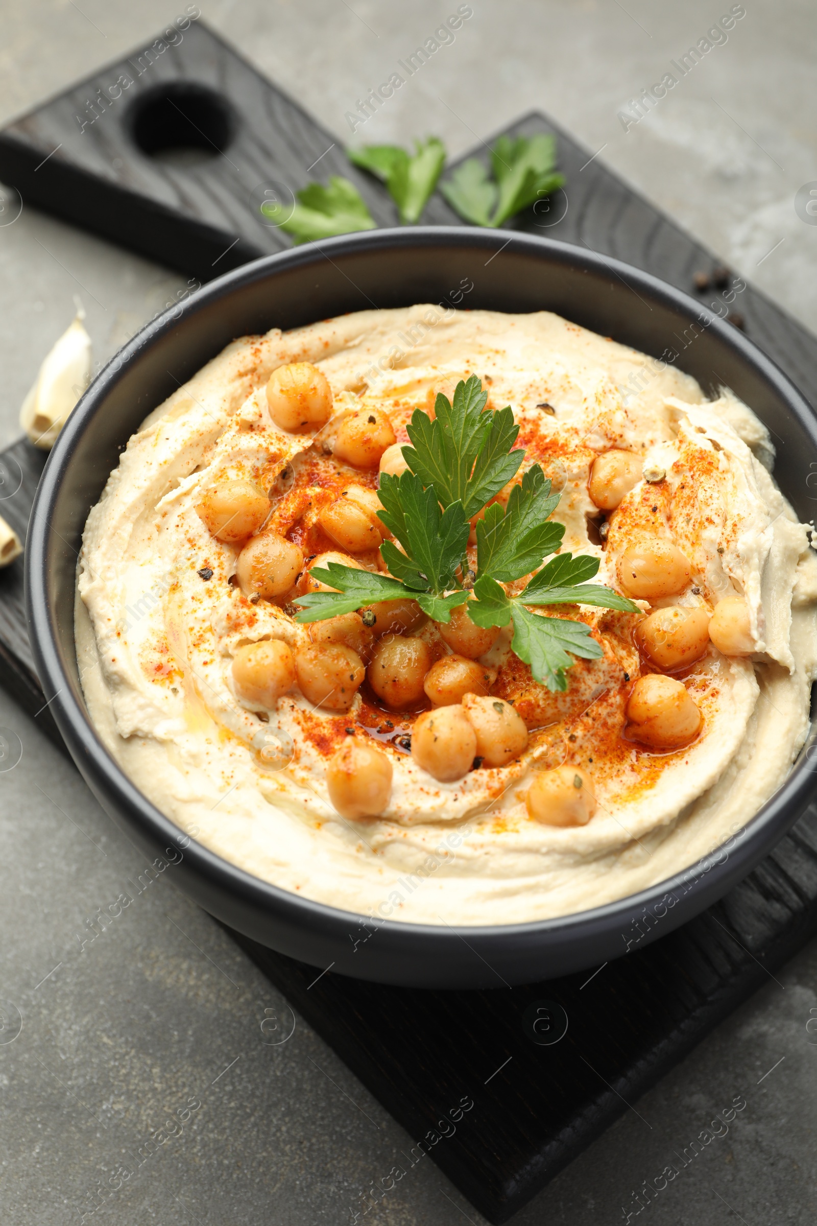 Photo of Delicious hummus with parsley, paprika and chickpeas on grey table, closeup