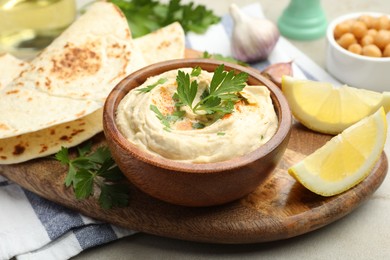 Photo of Delicious hummus with parsley, paprika, pita and lemon on grey table, closeup