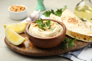 Photo of Delicious hummus with parsley, paprika, pita and lemon on grey table, closeup