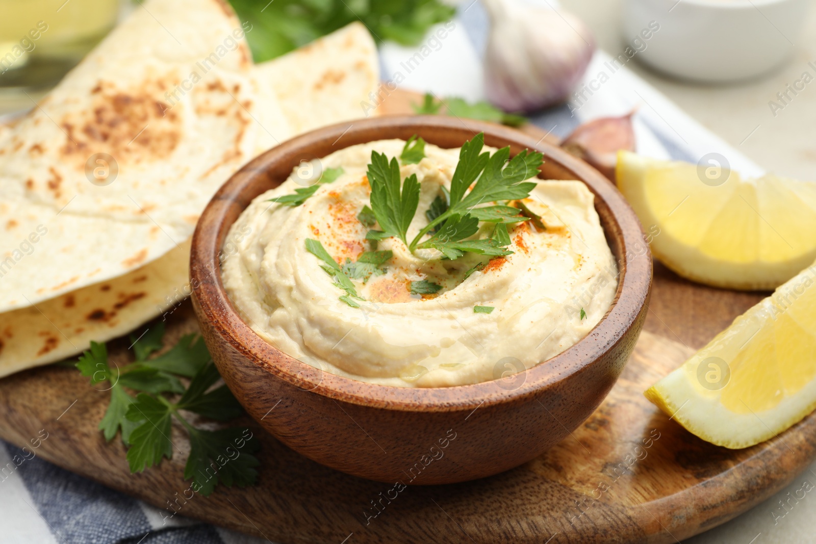 Photo of Delicious hummus with parsley, paprika, pita and lemon on table, closeup