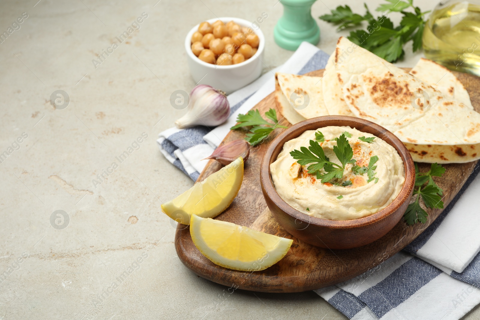 Photo of Delicious hummus with parsley, paprika, pita, chickpeas and lemon on grey table, space for text