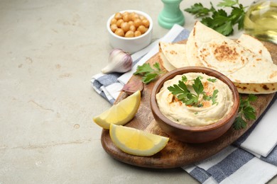 Photo of Delicious hummus with parsley, paprika, pita, chickpeas and lemon on grey table, space for text