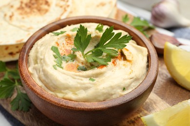 Photo of Delicious hummus with parsley, paprika, pita and lemon on table, closeup